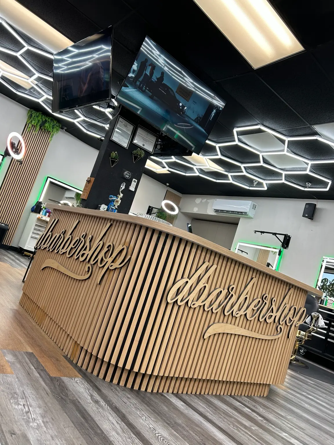 Curved wooden reception desk under hexagon ceiling lights at dbarbershop